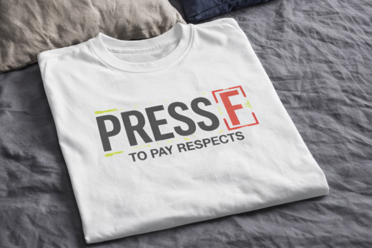 Weißes Gaming T-Shirt „Press F to Pay Respects“ flach ausgelegt neben schwarzem Shirt in Schlafzimmer-Szene