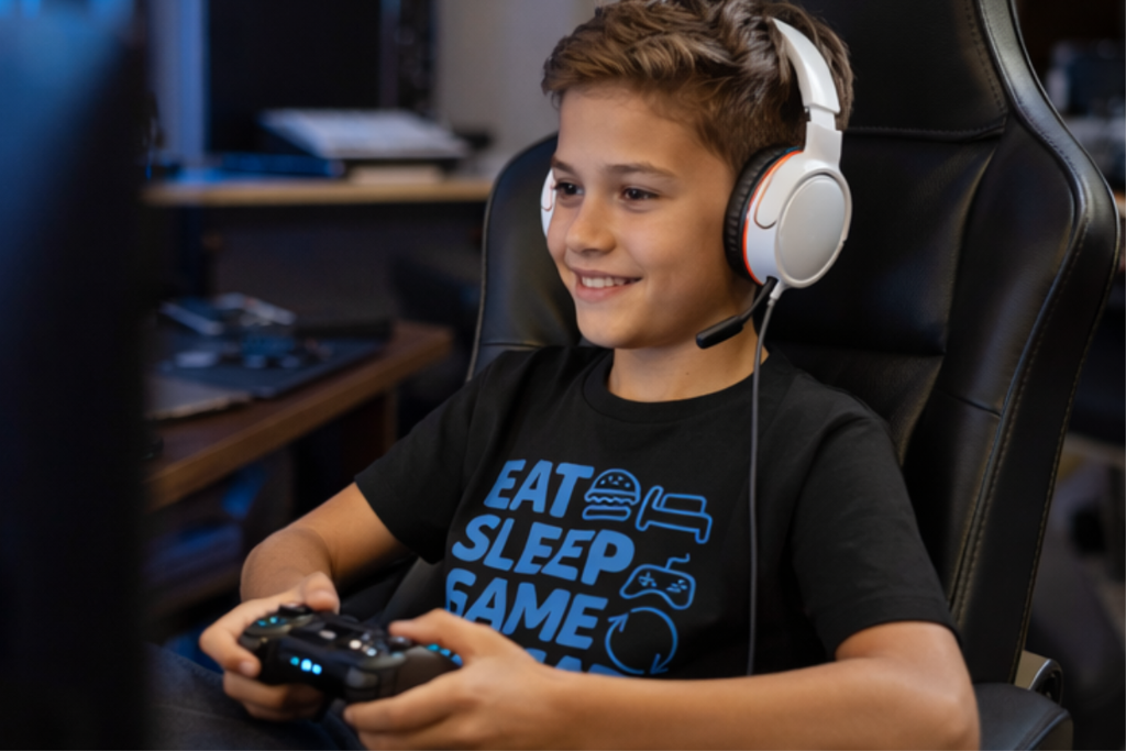 Kind spielt Videospiel mit Controller und trägt schwarzes „Eat Sleep Game Repeat“ Kinder T-Shirt