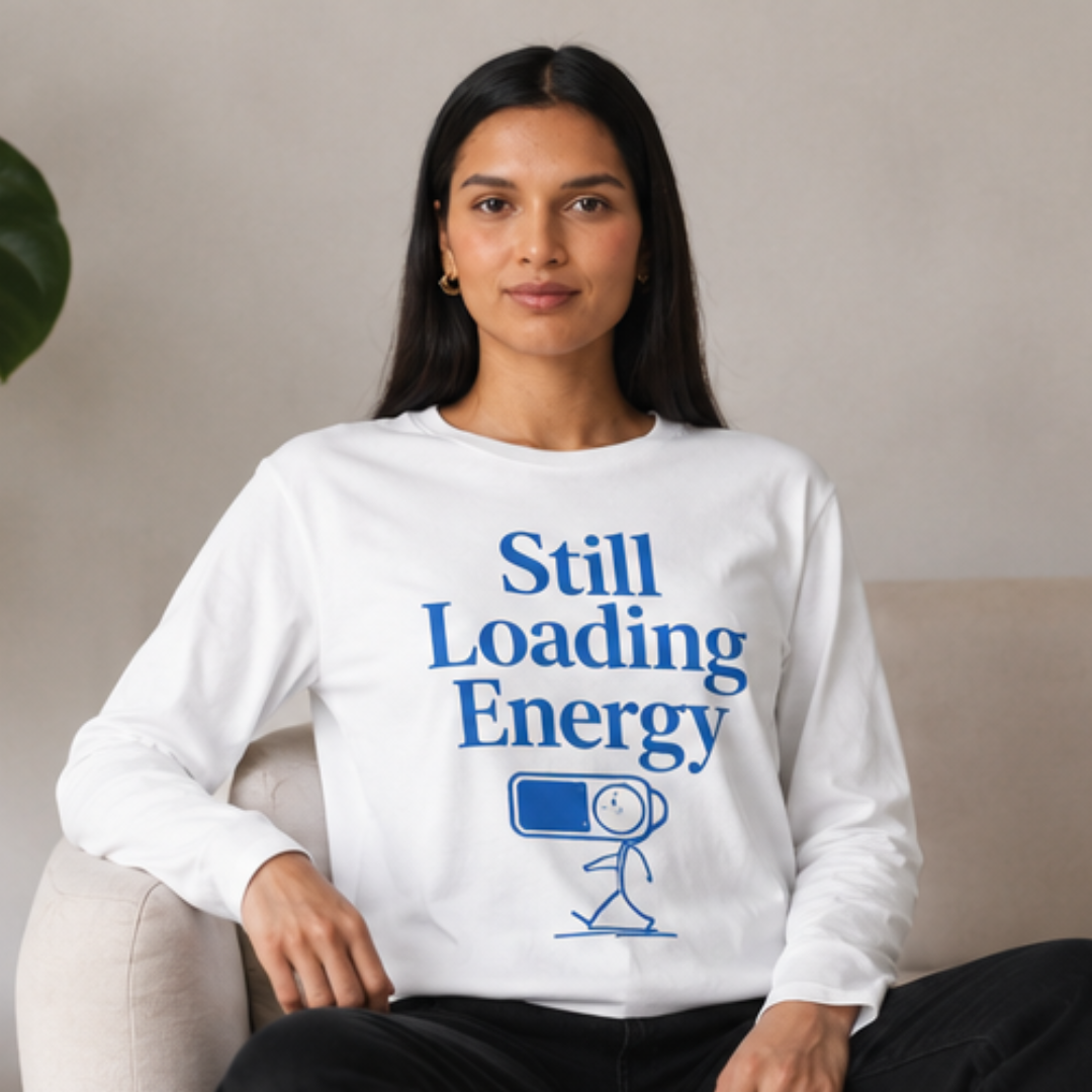 weibliches modell sitzt auf dem sofa. Weißes Longsleeve aus Bio-Baumwolle mit ‚Still Loading Energy‘ Design, frontal