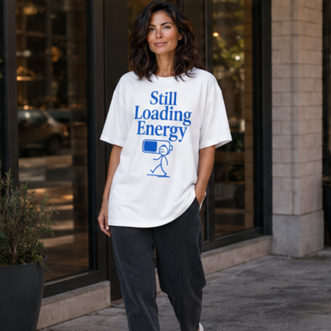 Weibliches Model trägt weißes Oversize T-Shirt mit blauem „Still Loading Energy“-Print, lockerer Unisex-Schnitt